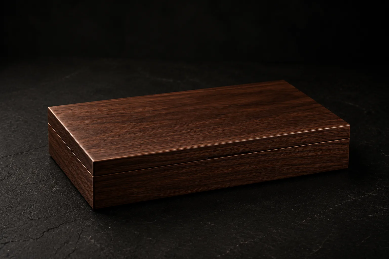 The closed Silent Ritual walnut box resting on dark slate, its grain catching a soft light.